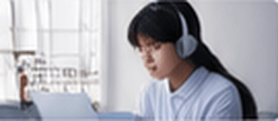 A learner wearing headphones, practicing with an AI tool on her laptop by a window